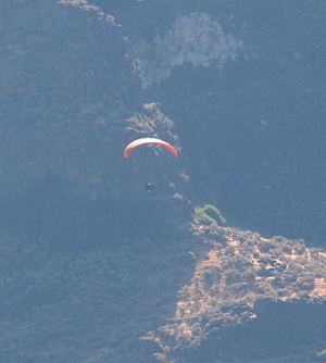 [A man is under canopy as he sits in a powered machine flying through the canyon.]